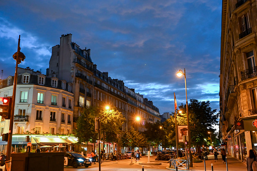 Paris,France,June 2022. View of a downtown crossroads at night. The buildings in typical Parisian style frame the street illuminated by the street lamps with yellow light. People on the street, a car.