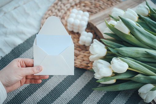 Hand with an empty envelope on a background of flowers, a place for your text.