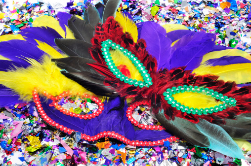 some carnival masks with feathers of different colors on a pile of confetti