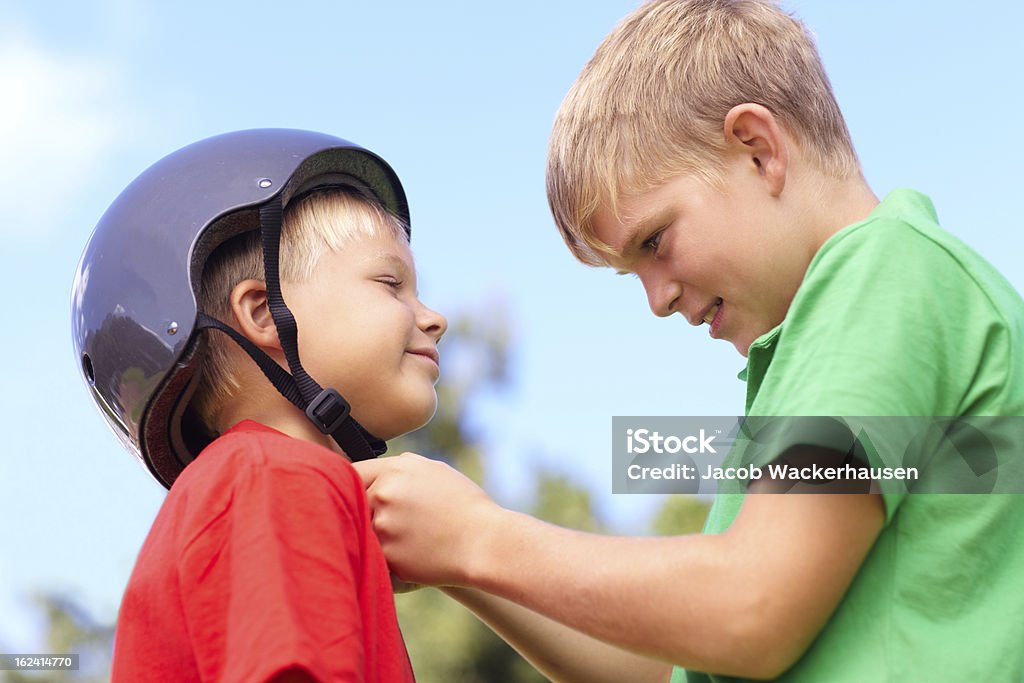 Making sure my little brother stays safe Young boy securing his little brother's cycling helmet Arm In Arm Stock Photo