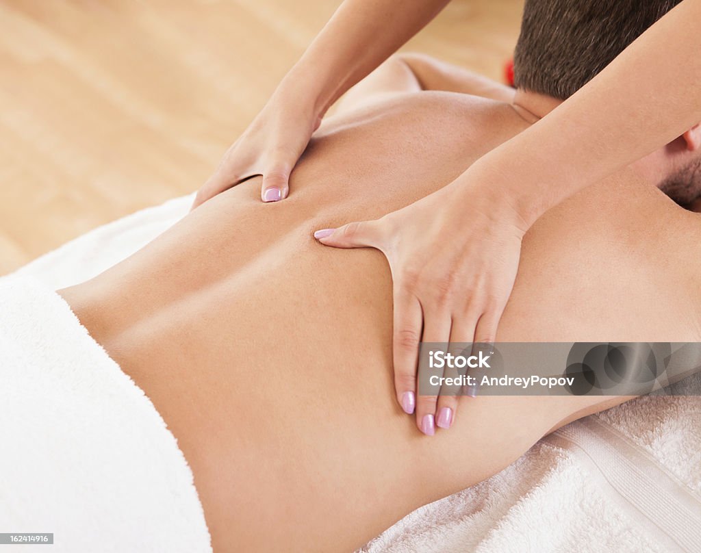 Man having a back massage Handsome young man lying on his stomach in a spa having a back massage Abdomen Stock Photo