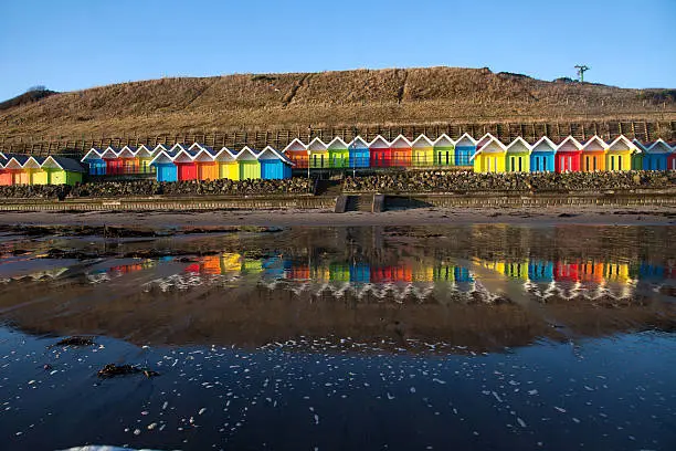 North Bay seafront Scarborough with highly coloured beach huts at sunrise with lots of dog walkers
