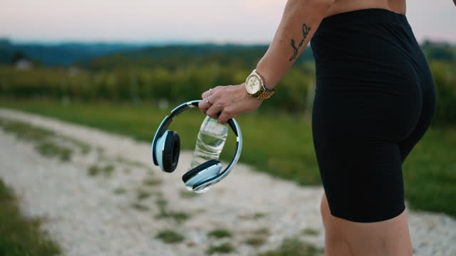SLO MO Female Runner Walking with Water Bottle and Wireless Headphones along Vineyard