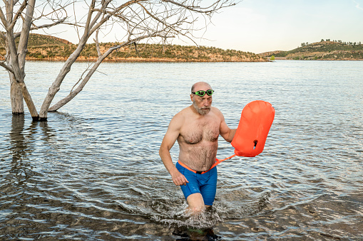 senior athletic, overweight man is finishing open water swimming with a swim buoy in a mountain lake,  Horsetooth Reservoir in northern Colorado