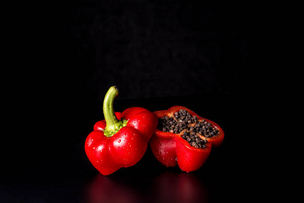 paprika rossa taglio asciutto in due con pepe nero interno - foto stock