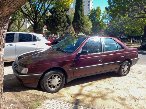 Buenos Aires, Argentina - Nov 11, 2022: Old red 1995 Peugeot 405 SRI saloon, sedan in the street in front of a park. Sunny day. Classic car.