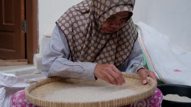 Female farmer cleans paddy in bamboo tray after milling