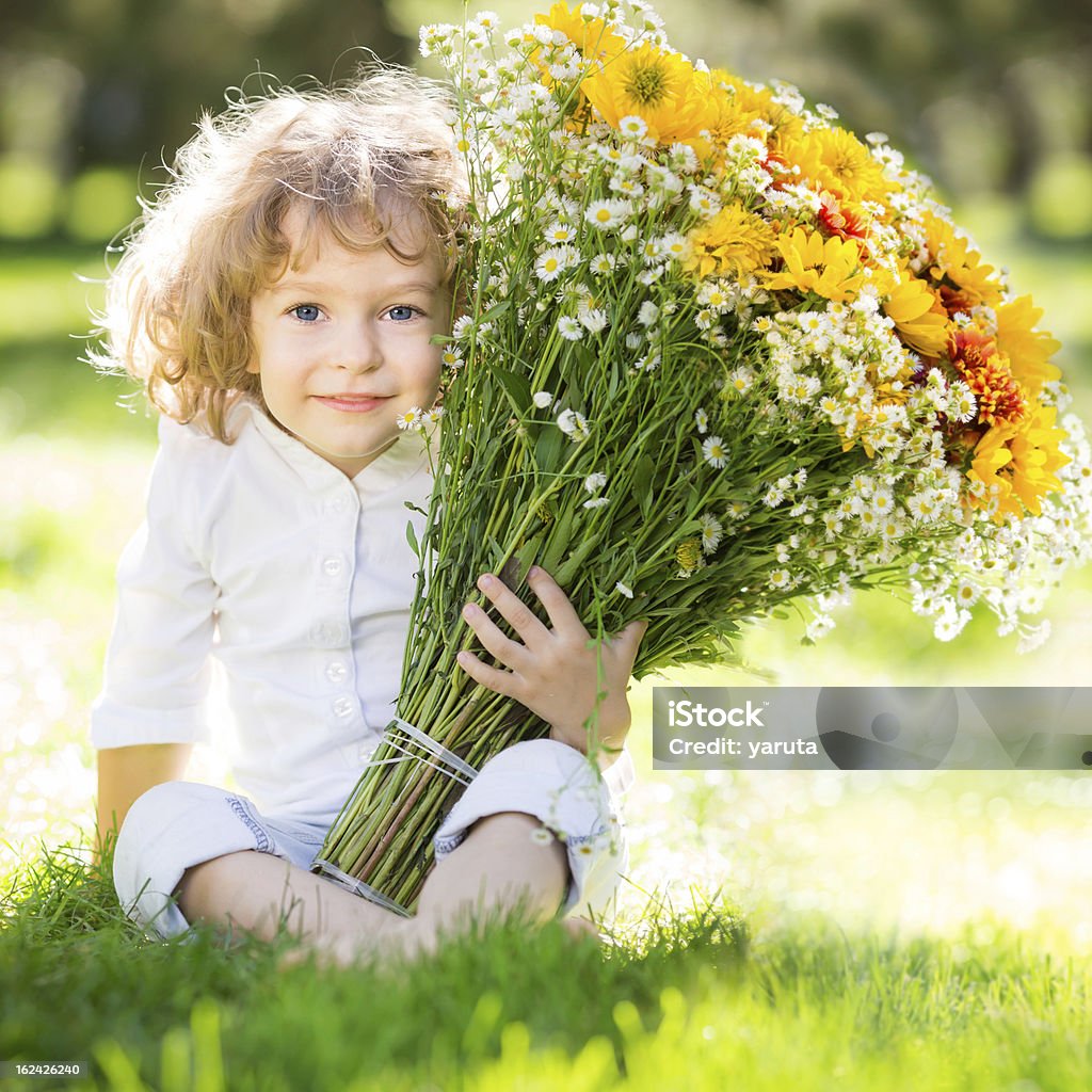 Child with flowers Happy child with bunch of flowers sitting on green grass in spring park Beautiful People Stock Photo