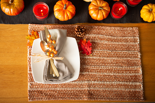 Thanksgiving table setting with golden cutlery and raffia ribbon on napkin on brown placemat