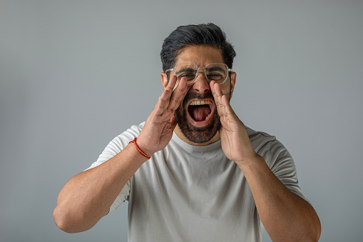Portrait of handsome mid adult man with hands covering mouth shouting in anger while standing against white background