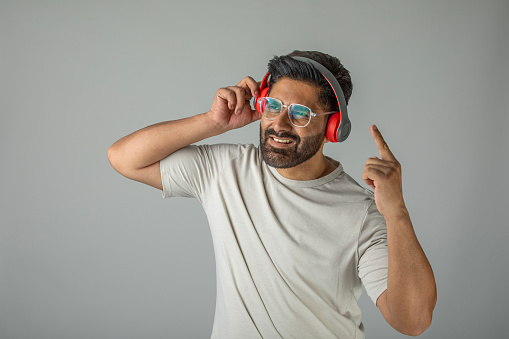 Portrait of senior man in headphones listening to music keeping eyes closed while standing against grey background