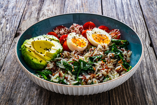 Cooked rice with avocado, spinach, boiled eggs and cherry tomatoes on wooden background