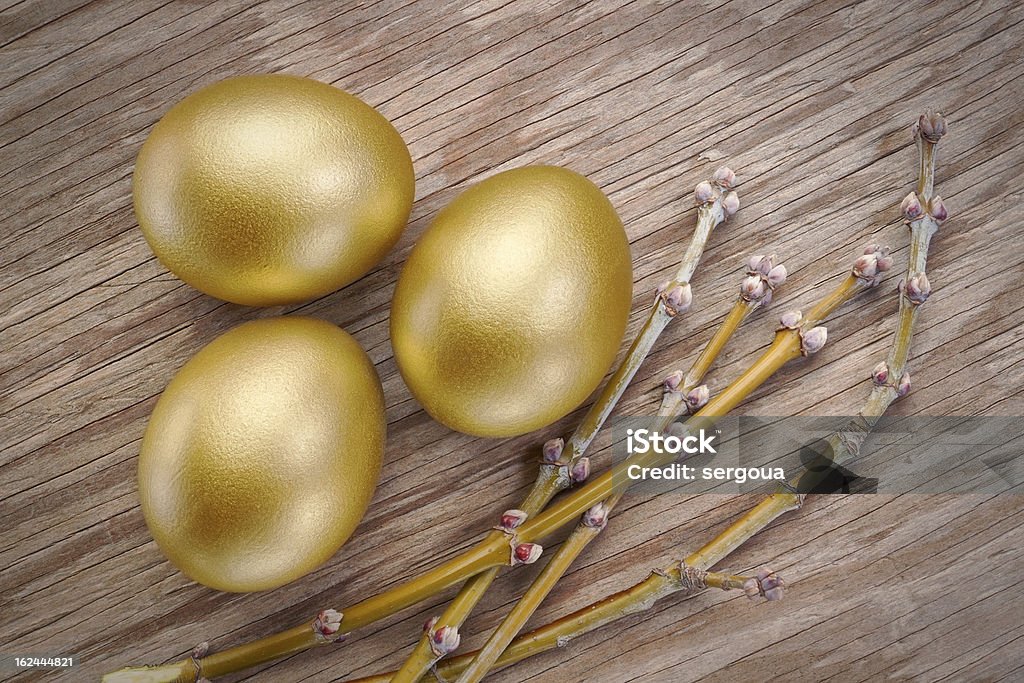 Three gold eggs and spring branch at Easter. Three gold eggs and spring branch at Easter. On a wooden texture. Animal Egg Stock Photo