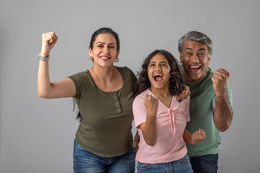 Portrait of cheerful Indian parents with daughter shaking fists and screaming ecstatically against white background