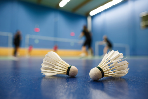badminton courts with players competing; shuttlecocks in the foreground (shallow DOF; color toned image)