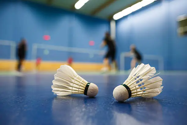 Photo of Blue badminton court and shuttlecocks with players competing