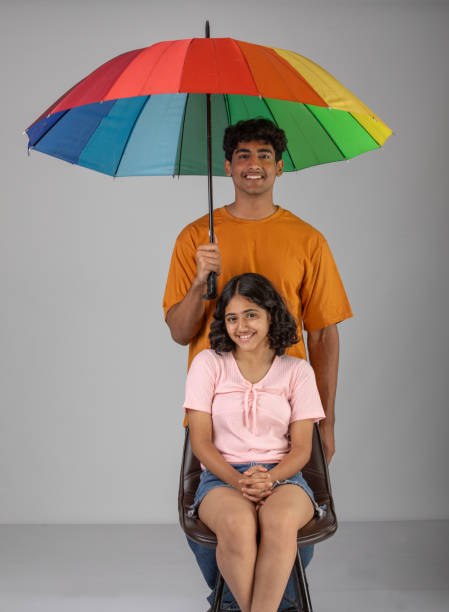 istock Smiling siblings with umbrella against white background 1624465209