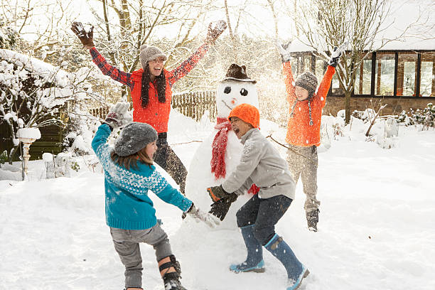 Happy mom and children building snowman in yard stock photo