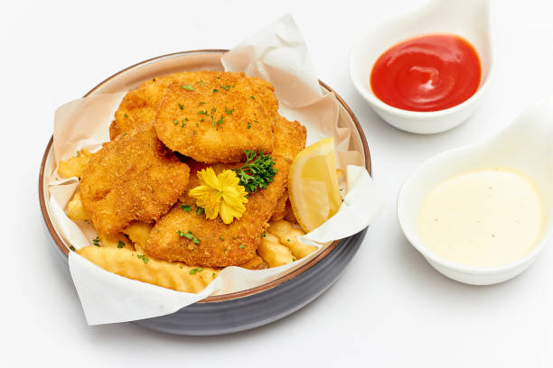 Fish and Chips (battered fish and fries potato) served in a large bowl decorated with flowers and parsley and dipping sauce (ketchup and mayonnaise) isolated on white background.