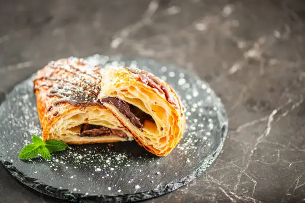 Freshly baked croissant filled with dark chocolate, topped with chocolate flavoured fondant and dusted with icing sugar
