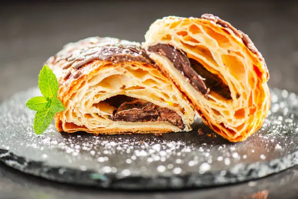 Freshly baked croissant filled with dark chocolate, topped with chocolate flavoured fondant and dusted with icing sugar