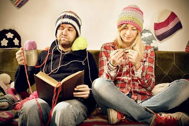 Annoying young knitter woman couple portrait on couch with winter hats