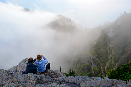 A young guy and girl sit on a ledge at sunset and enjoy the scenery in the Great Smoky Mountains National Park