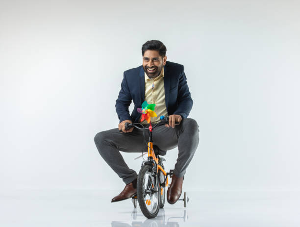 Cheerful senior businessman dressed in elegant suit riding bicycle against white background