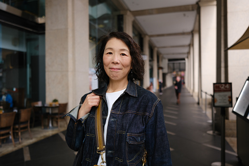 Smiling Asian woman in denim jacket walking in an arcade.