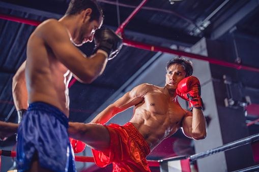 One young man, kick boxer, with boxing gloves punching a punching bag in the gym.