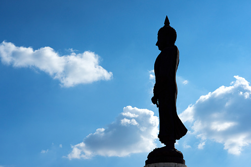 Silhouette of large Buddha statue and blue sky with white clouds