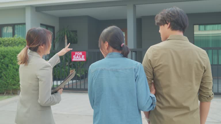 Young Asian woman real estate broker showing house to client buyers outside at home. Buying a new house.