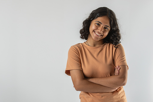 Portrait of confident smiling teenage girl with arms crossed standing isolated against white background