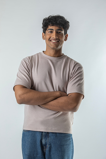 Portrait of confident smiling teenage boy with arms crossed standing isolated against white background