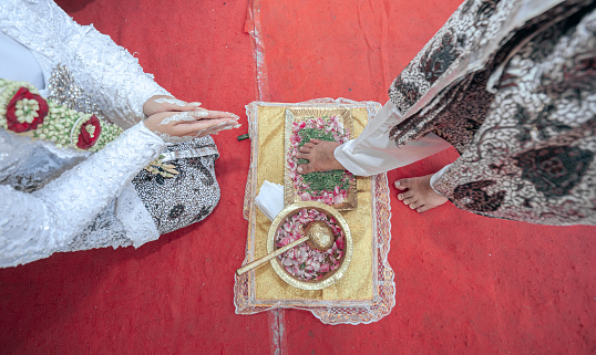 Javanese traditional wedding ceremony. Top view of the groom's right foot stepping on the egg in front of the bride.