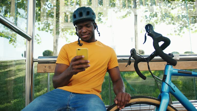 African American uses phone sitting at bus stop near bike