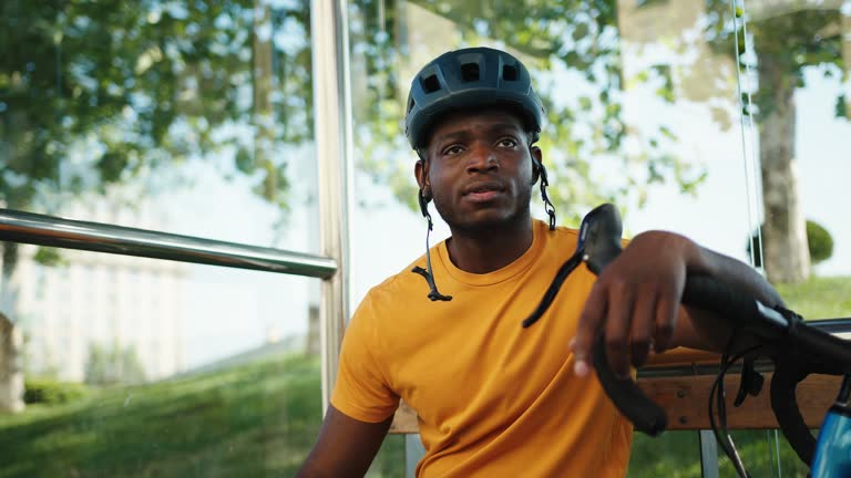 Positive African American man sits at bus stop with bicycle