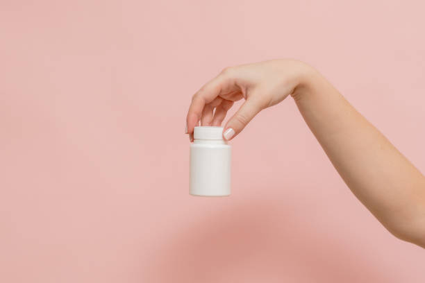 istock Plastic bottle (tube) in hand on pink background. Packaging for vitamins, tablets or capsule, or supplement 1624859756