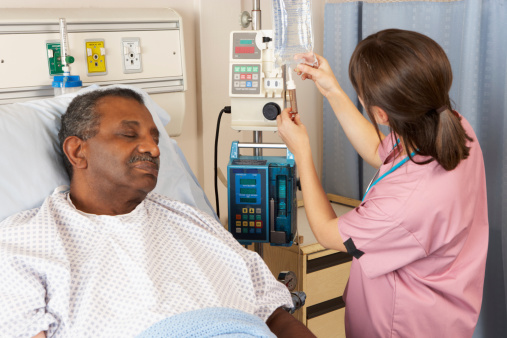 Female Nurse Checking Senior Male Patient's IV Drip On Ward
