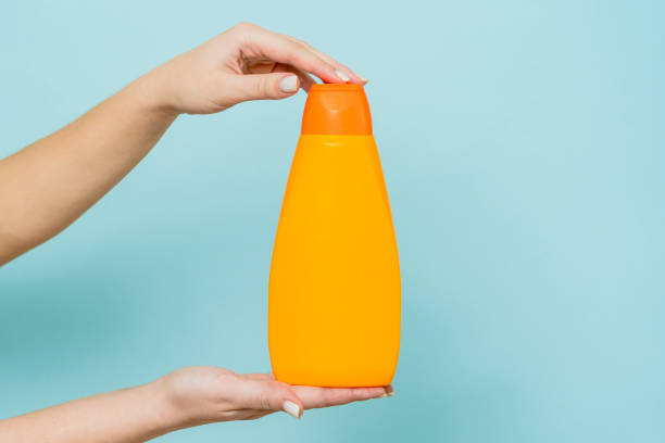istock Woman's hand holding packaging of shampoo or conditioner on blue background. Copy space and mock up 1624860841