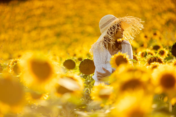 Beautiful young carefree woman wearing white dress and enjoying on sunflower field at summer.