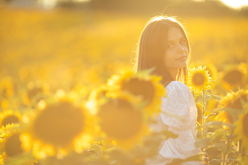 Beautiful young carefree woman wearing white dress and enjoying on sunflower field at summer.