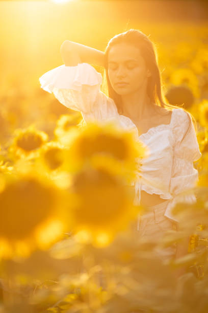 Beautiful young carefree woman wearing white dress and enjoying on sunflower field at summer.