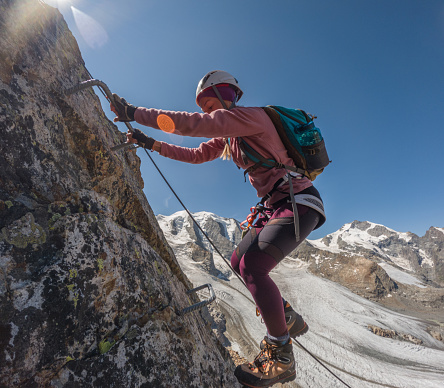 Wide angle view of sporty female climbing in summer on Via Ferrata in Switzerland. Glacier in distance