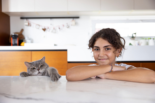 On the marble countertop, a smiling young girl spends time with her adorable chubby cat.