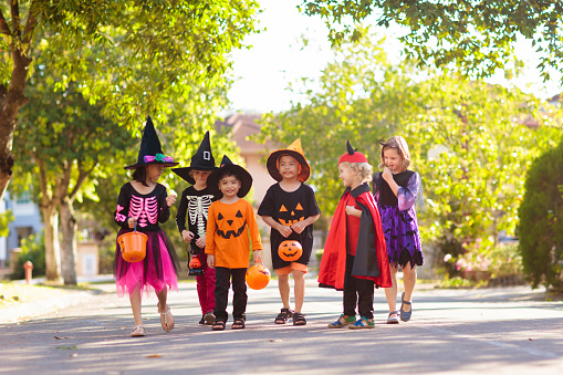 Child in Halloween costume. Mixed race Asian and Caucasian kids trick or treat on suburban street. Little boy and girl with pumpkin lantern and candy bucket. Baby in witch hat. Autumn holiday fun.