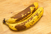 Ripe bananas with a brown peel lying on a wooden kitchen counter