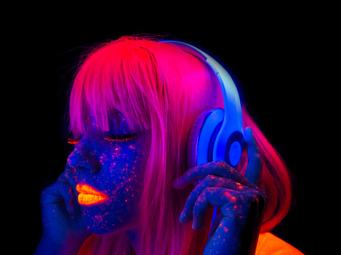 Futuristic woman with headphones listening to the music with painted face with neon lights