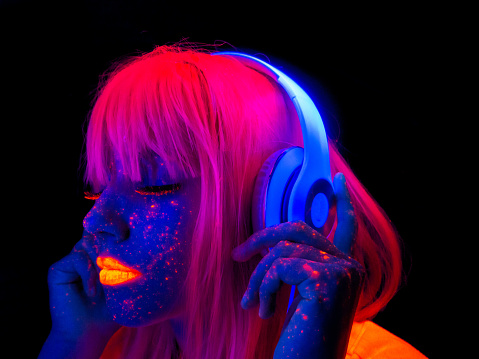 Futuristic woman with headphones listening to the music with painted face with neon lights