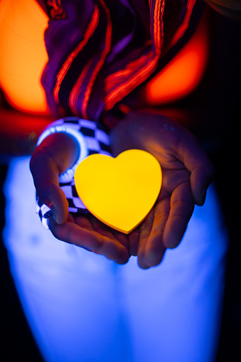 Woman holding a heart shape in her hands under neon lights